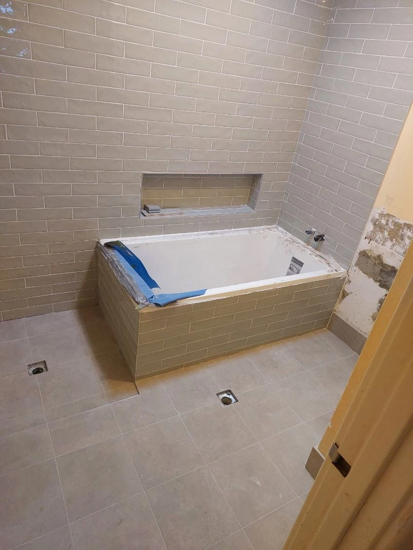 Grey wall and floor tiles around a protected built-in bath